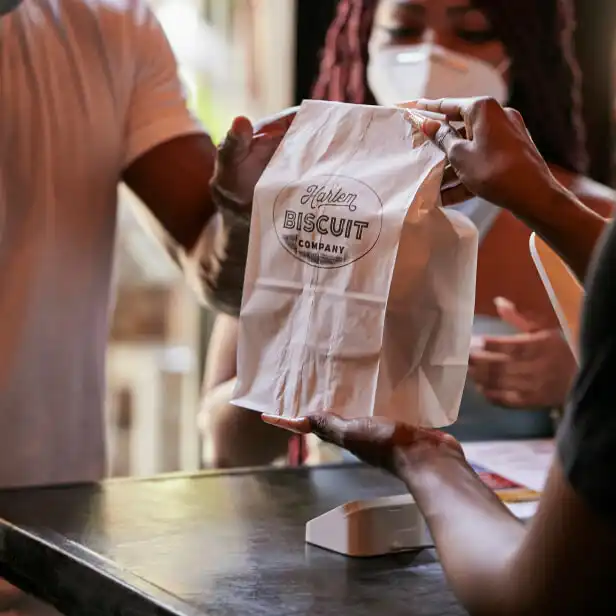 Harlem biscuit company employee hands bag of biscuits to patron